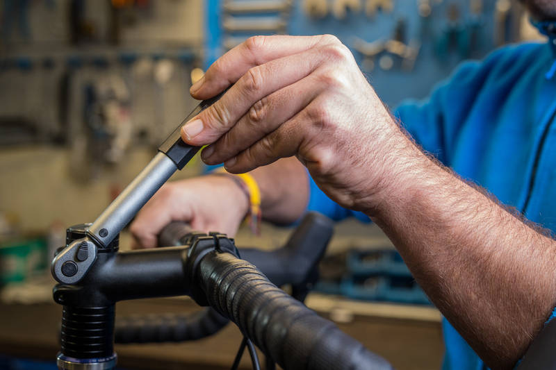 Hands of bicycle mechanic tightening the stem steerer clamp bolts of a bicycle using a torque wrench.